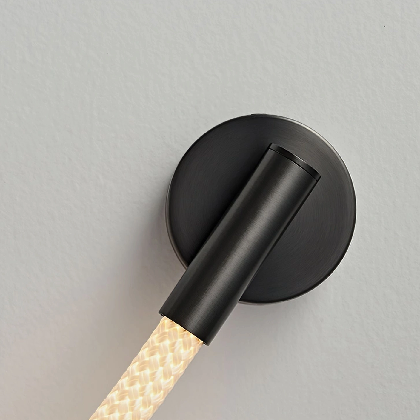 Close-up side angle detail of Flecto Tube wall lamp mounting system showing brushed black metal base and silicone rope connection