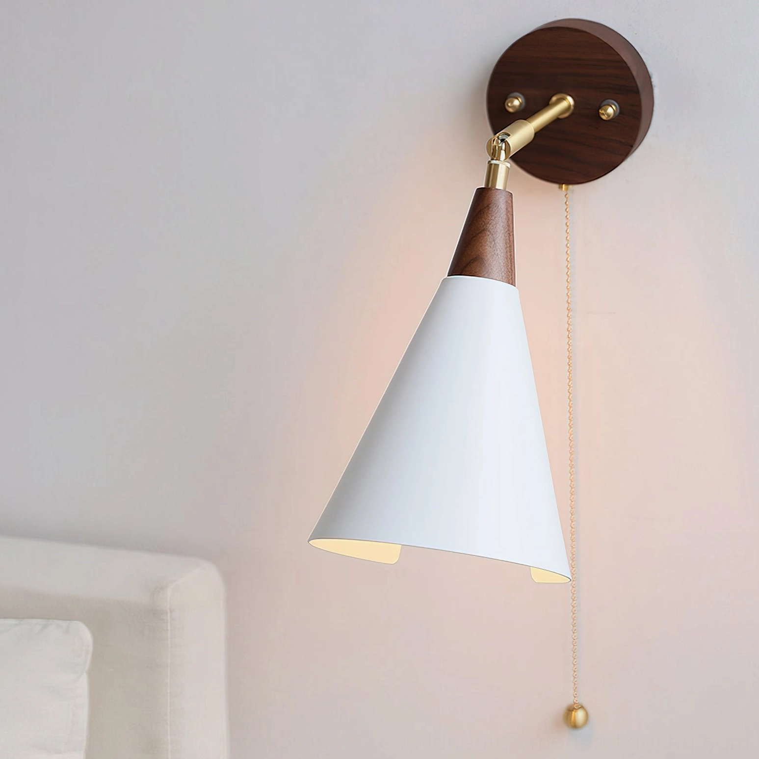 Fleka wall-mounted reading lamp angled downward, showing conical white shade and brass hardware articulation details