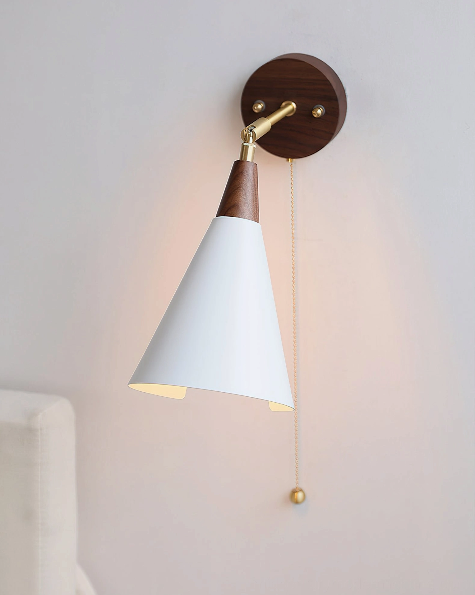 Fleka bedside wall light fully assembled and illuminated, downward-angled white shade, viewed from below against bedroom sofa
