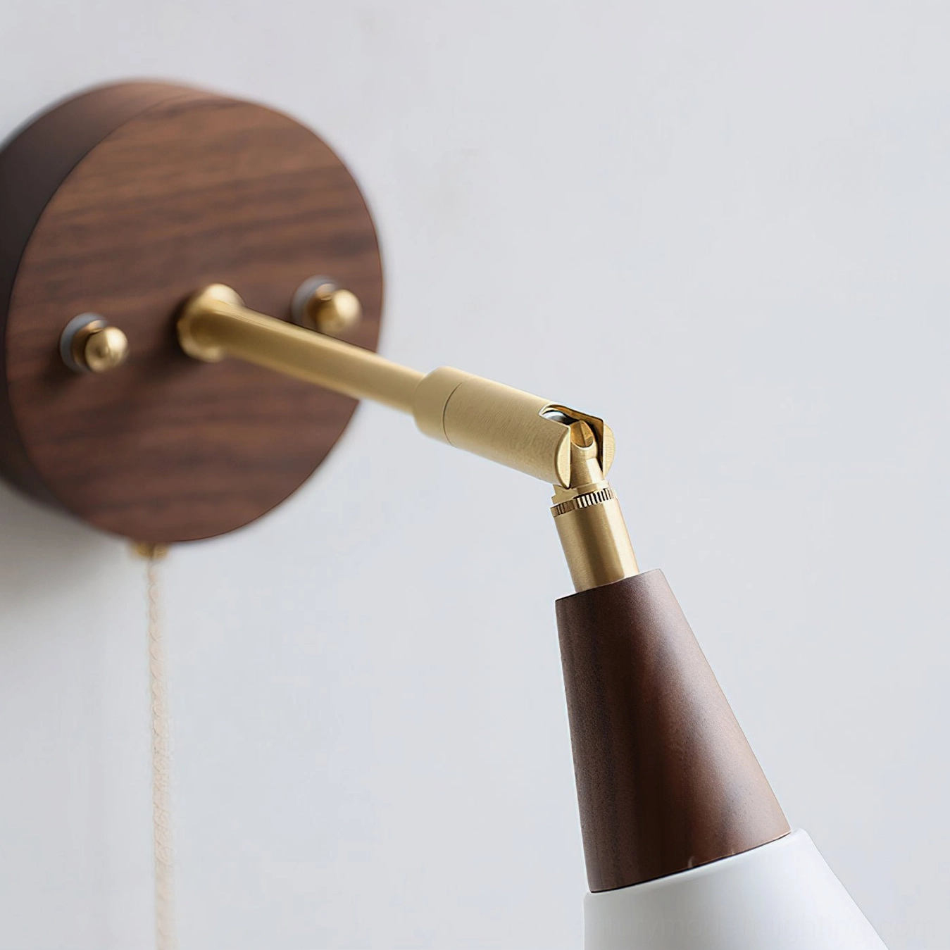 Close-up detail shot of Fleka wall sconce hardware including adjustable brass joint, walnut mounting plate, and cord mechanism