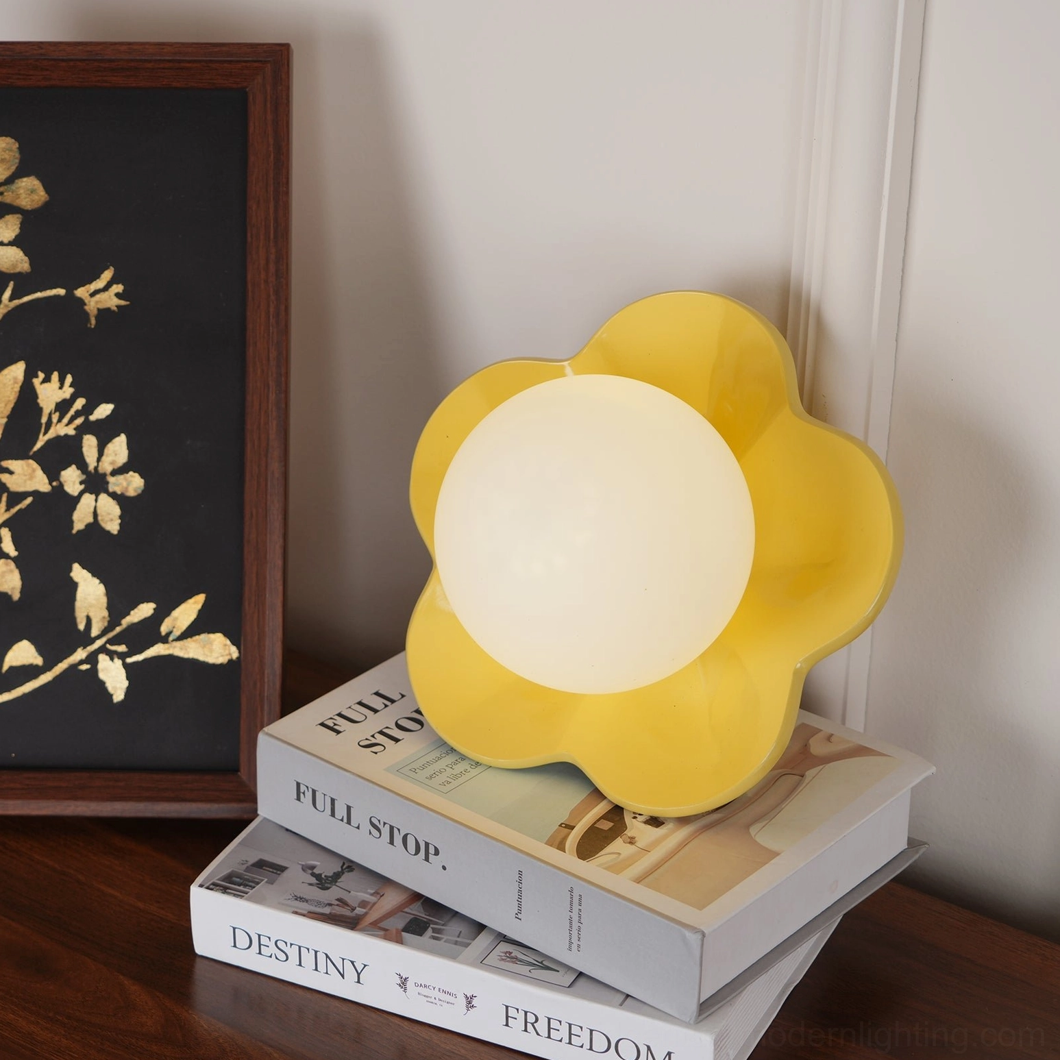 Yellow resin flower lamp at three-quarter angle on wooden table with book and frame styling
