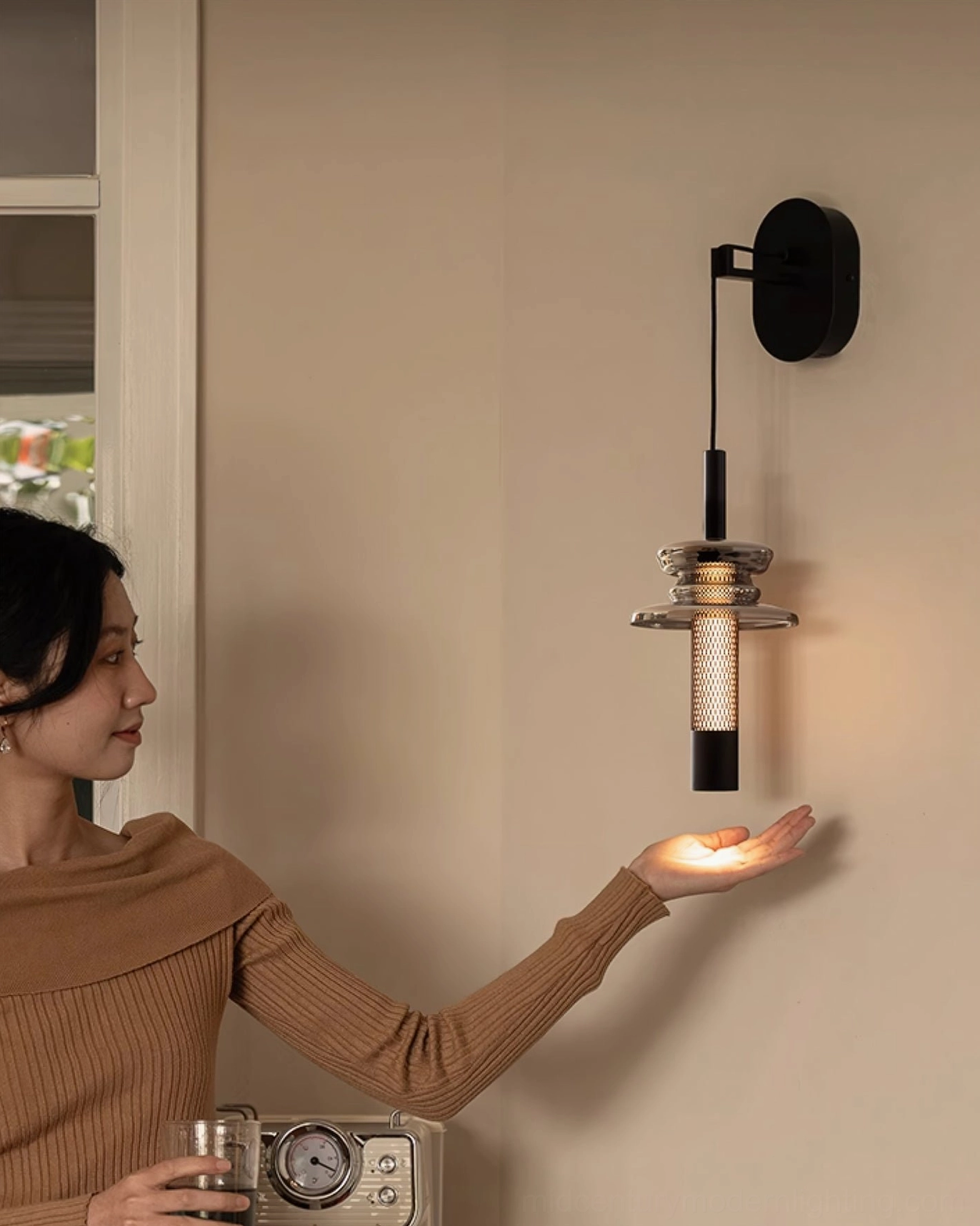 Float wall light with hand demonstrating soft diffused light output through glass and metal