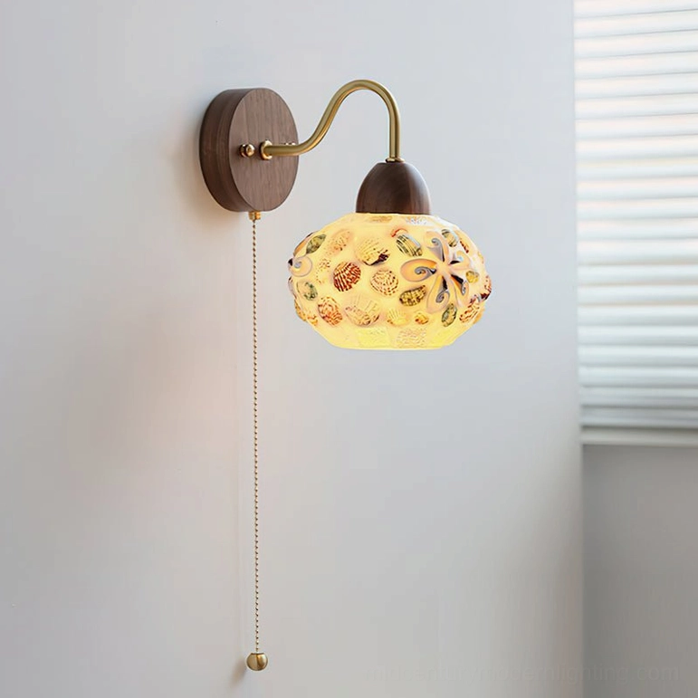 Embossed wall lamp with floral glass shade and brass pull chain mounted on bedroom wall - close-up side view
