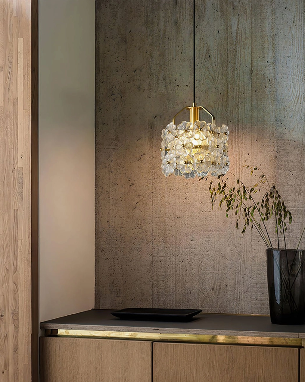 Elegant glass flower pendant displayed above cabinet with potted plant in textured interior wall space