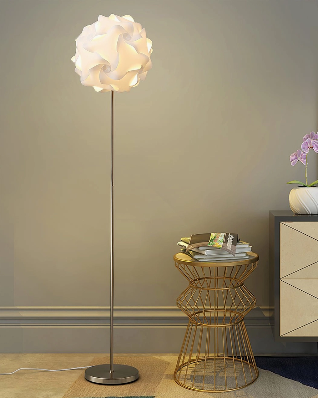 Flower floor lamp with silver stand and white shade beside gold wire side table and decorative cabinet