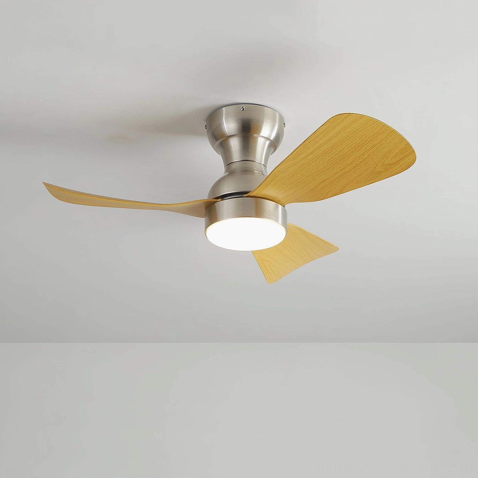 Integrated LED ceiling fan light installed flush to white ceiling, bottom-up perspective showing light wood blades and round LED lamp module in empty room