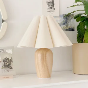 Beige pleated fabric table lamp displayed on home shelf with three-quarter angle view in boho minimalist interior styling