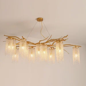 Forest Dawn Chandelier lit with warm golden illumination showing natural branch-shaped brass frame against neutral wall