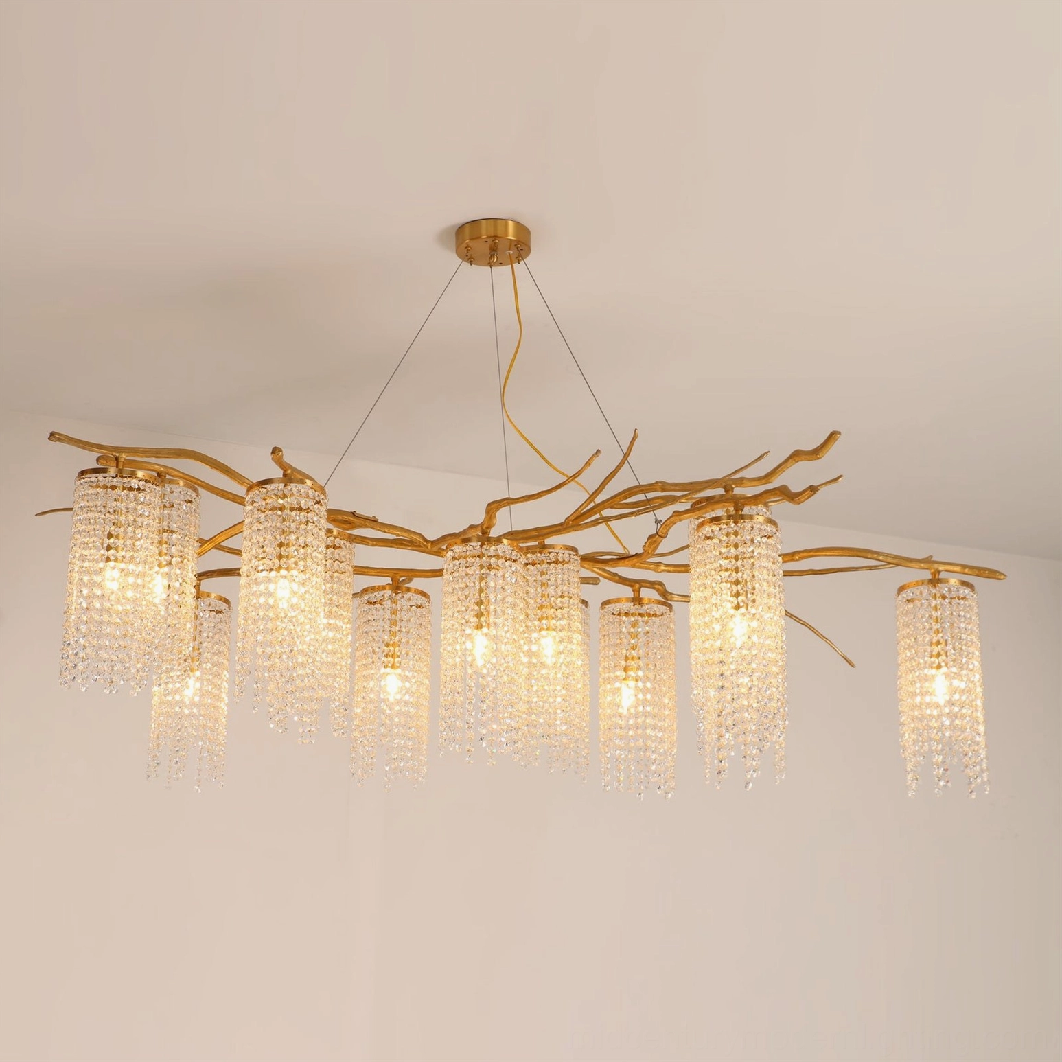 Forest Dawn Chandelier lit with warm golden illumination showing natural branch-shaped brass frame against neutral wall