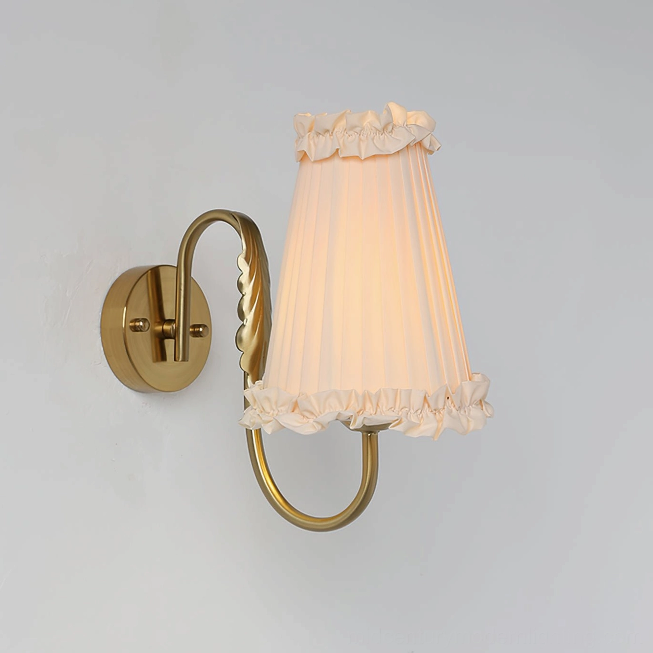 Curved brass arm wall lamp with pleated beige fabric shade and ruffled trim - side angle view