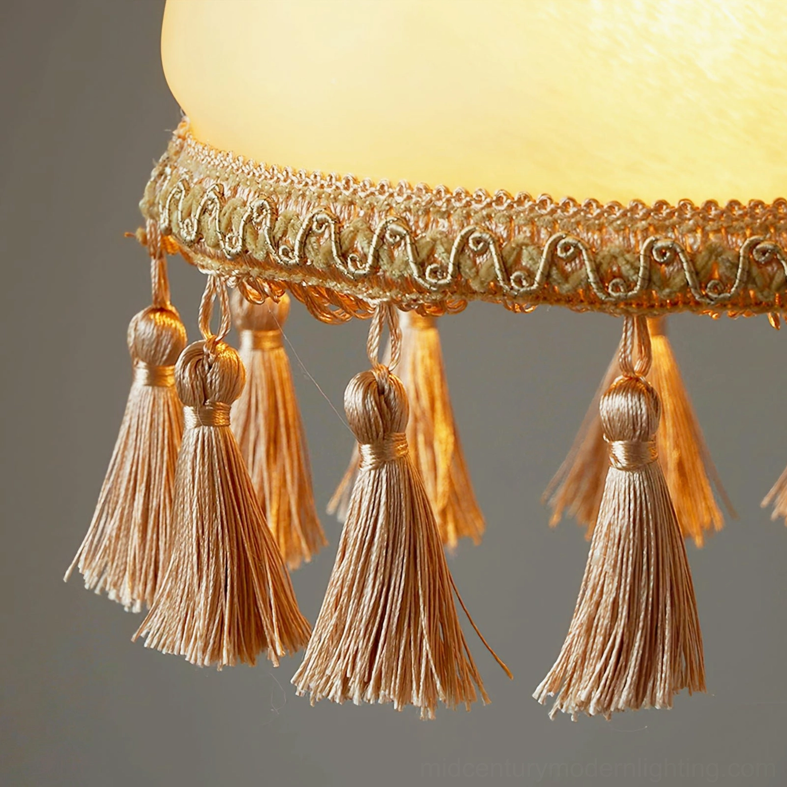 Bottom tassel detail of French brass pendant showing embroidered lace and fabric tassels in brown and beige