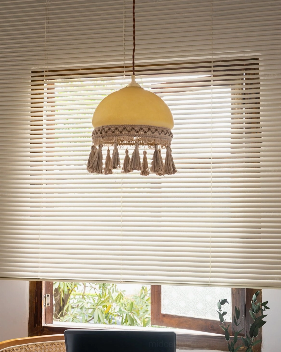 Minimalist bohemian French tassel pendant light hanging by window blinds in clean workspace