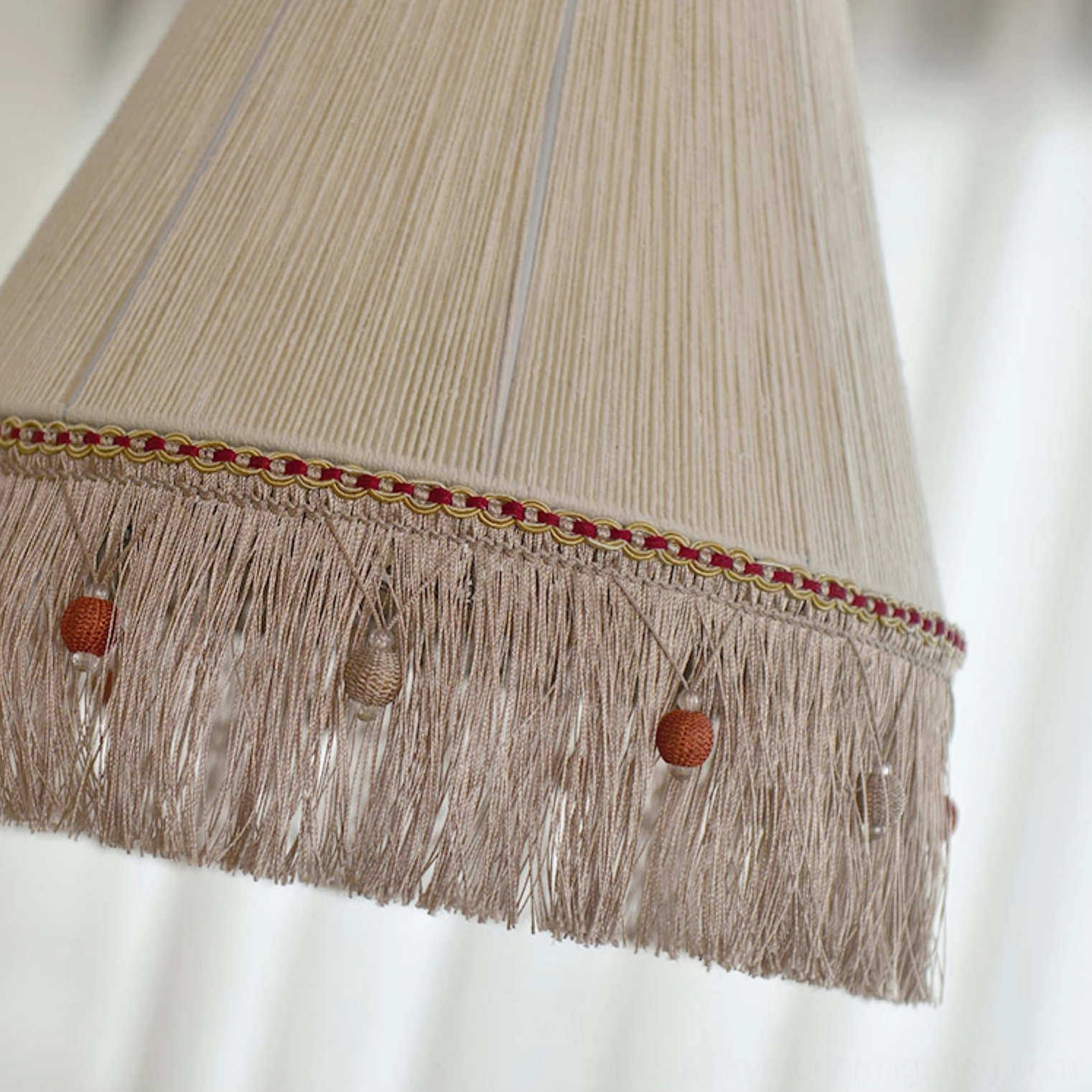 Close-up detail of beige cotton woven shade with decorative tassel and bead trim underside view