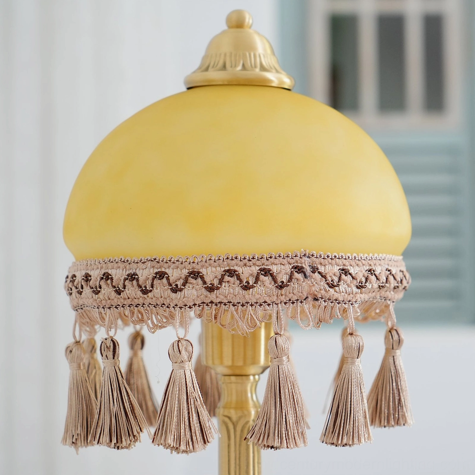 Top-down view of brass table lamp frosted glass dome, tassel trim, and brass finial