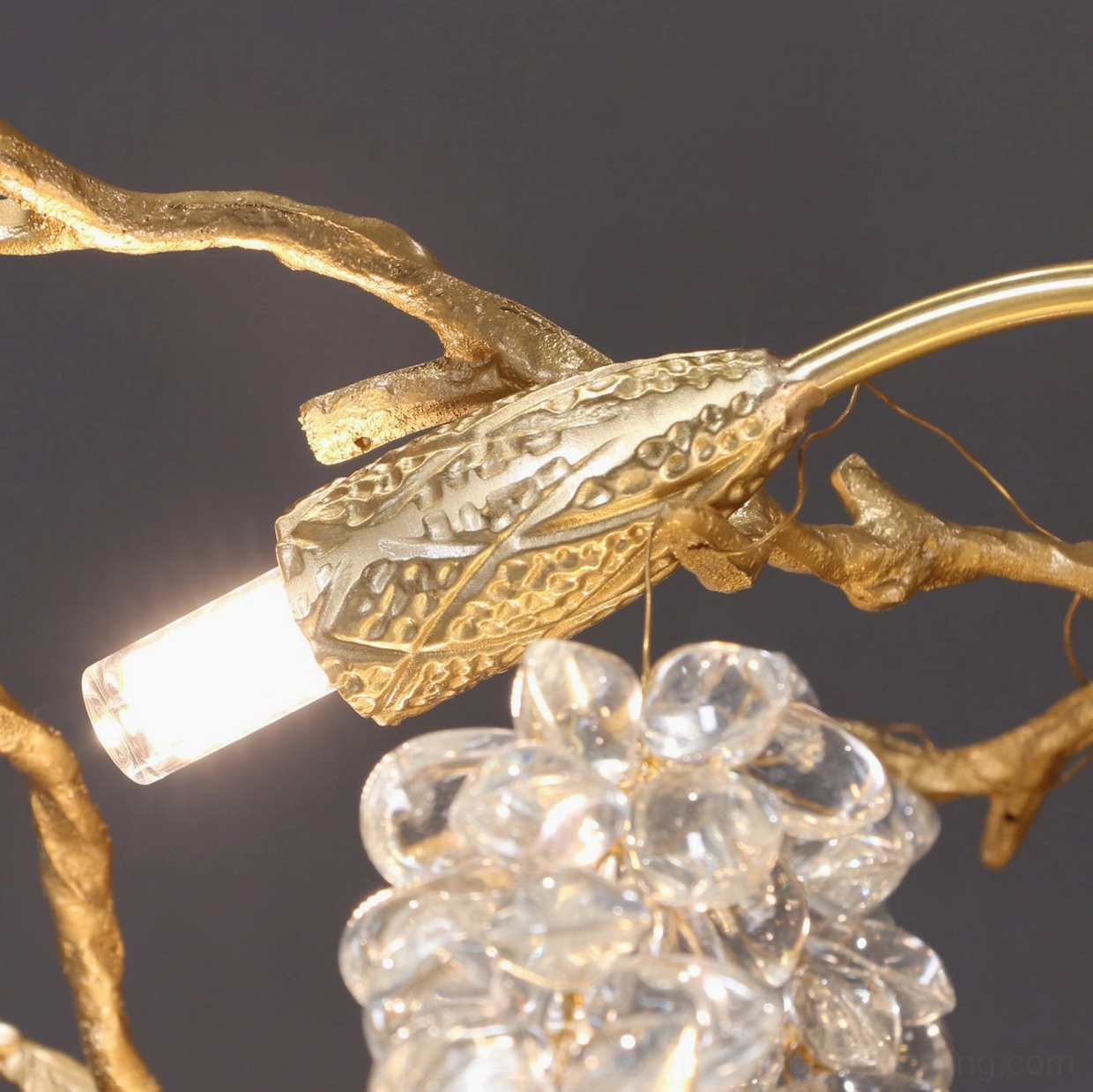 Close-up of G9 light socket on embossed gold metal branch with exposed bulb and crystal grape pendants on dark background