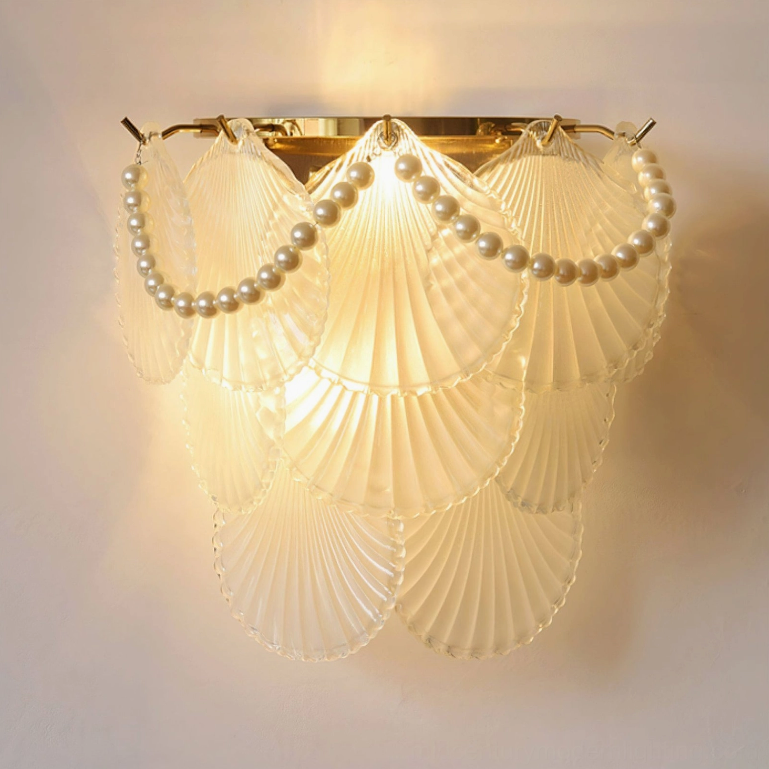 Galerie modern wall lamp close-up showing clear glass shell, pearl trim, and warm gold lighting