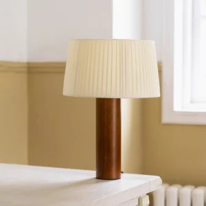 Mid-century modern wooden table lamp with dark walnut base and pleated shade on yellow wall interior, three-quarter view