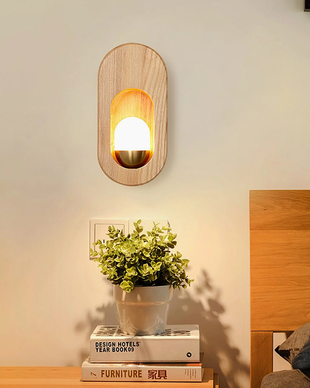 Geometric wooden wall lamp above bedroom shelf with potted plant and stacked books below