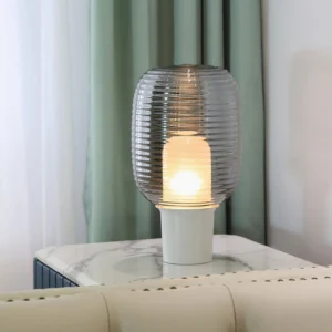 Ghia smoke grey ribbed glass table lamp in modern living room with marble side table and green curtain backdrop
