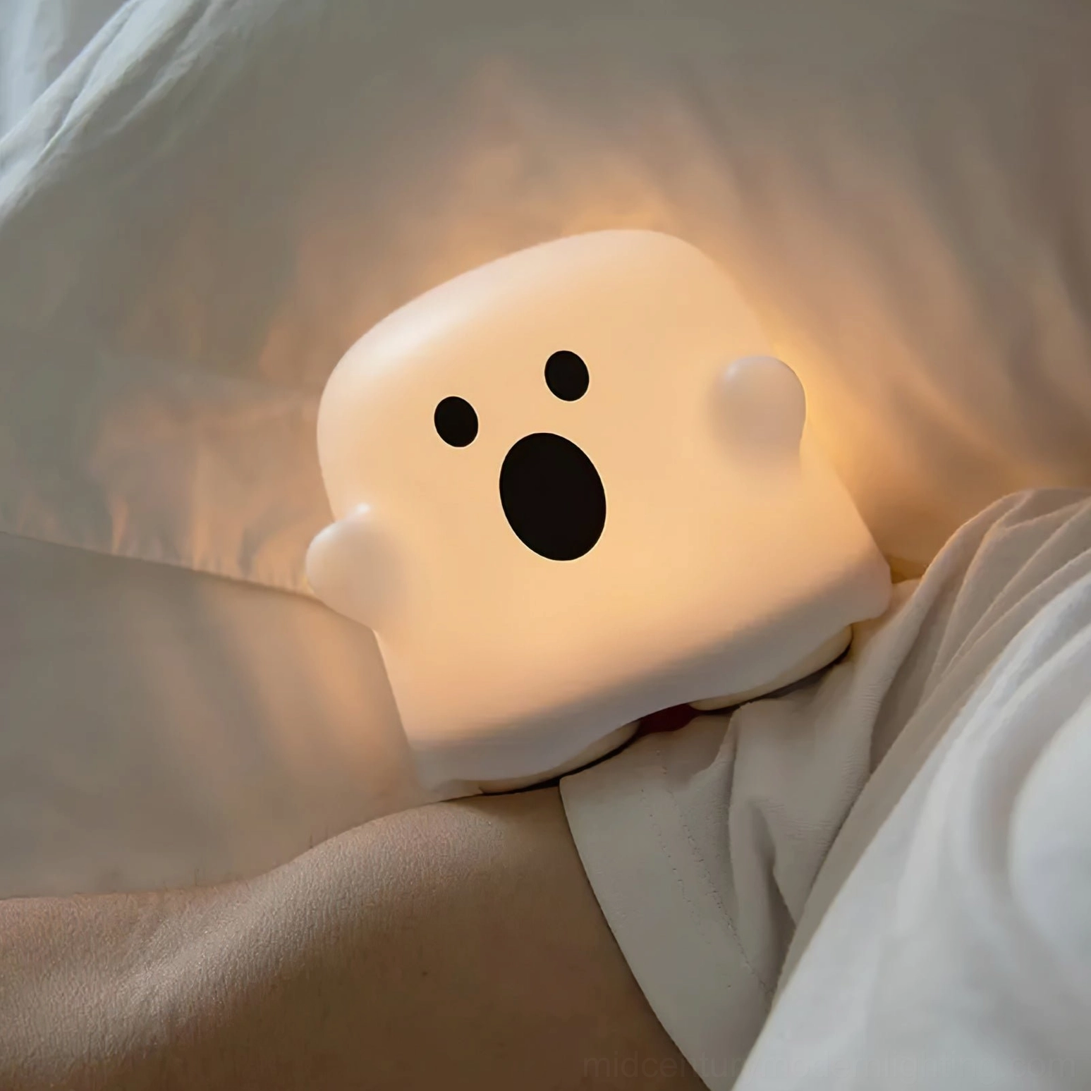 Ghost night light close-up side view glowing warm ambient light on bedroom bed with soft silicone texture