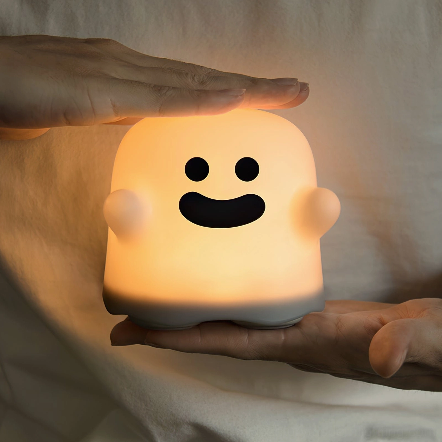 Ghost night light with cheerful expression placed on palm showing portable cordless design warm ambient glow