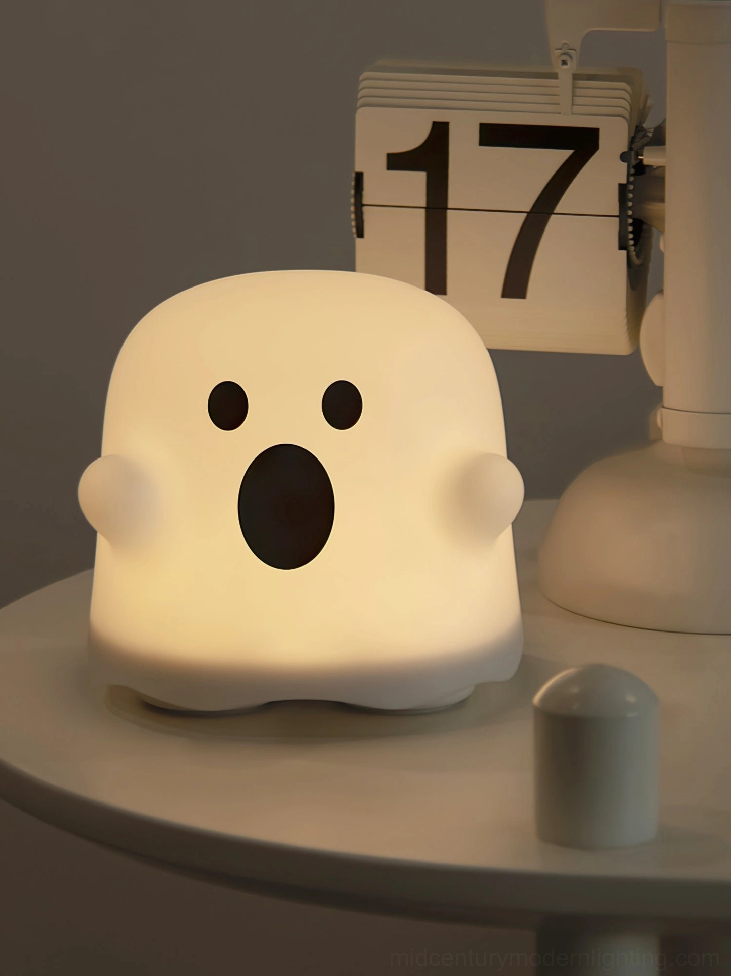 Illuminated ghost silicone night light with surprised expression on bedroom side table next to flip clock