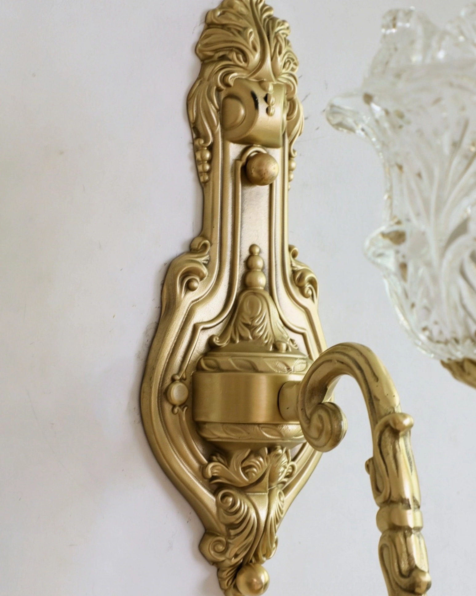 Side close-up of Gideon Baroque wall sconce bracket highlighting intricate Baroque carved details and brushed brass finish on white wall