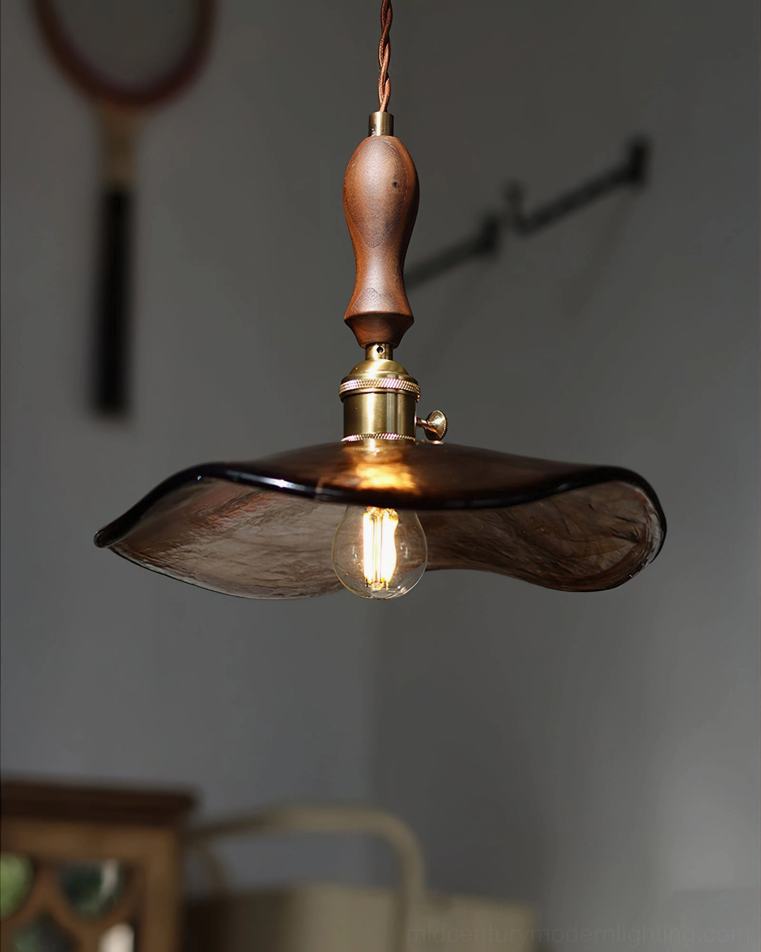 Close-up detail of Gideon pendant showing hand-blown amber glass texture, solid walnut wood finial, and aged brass fixture in soft light