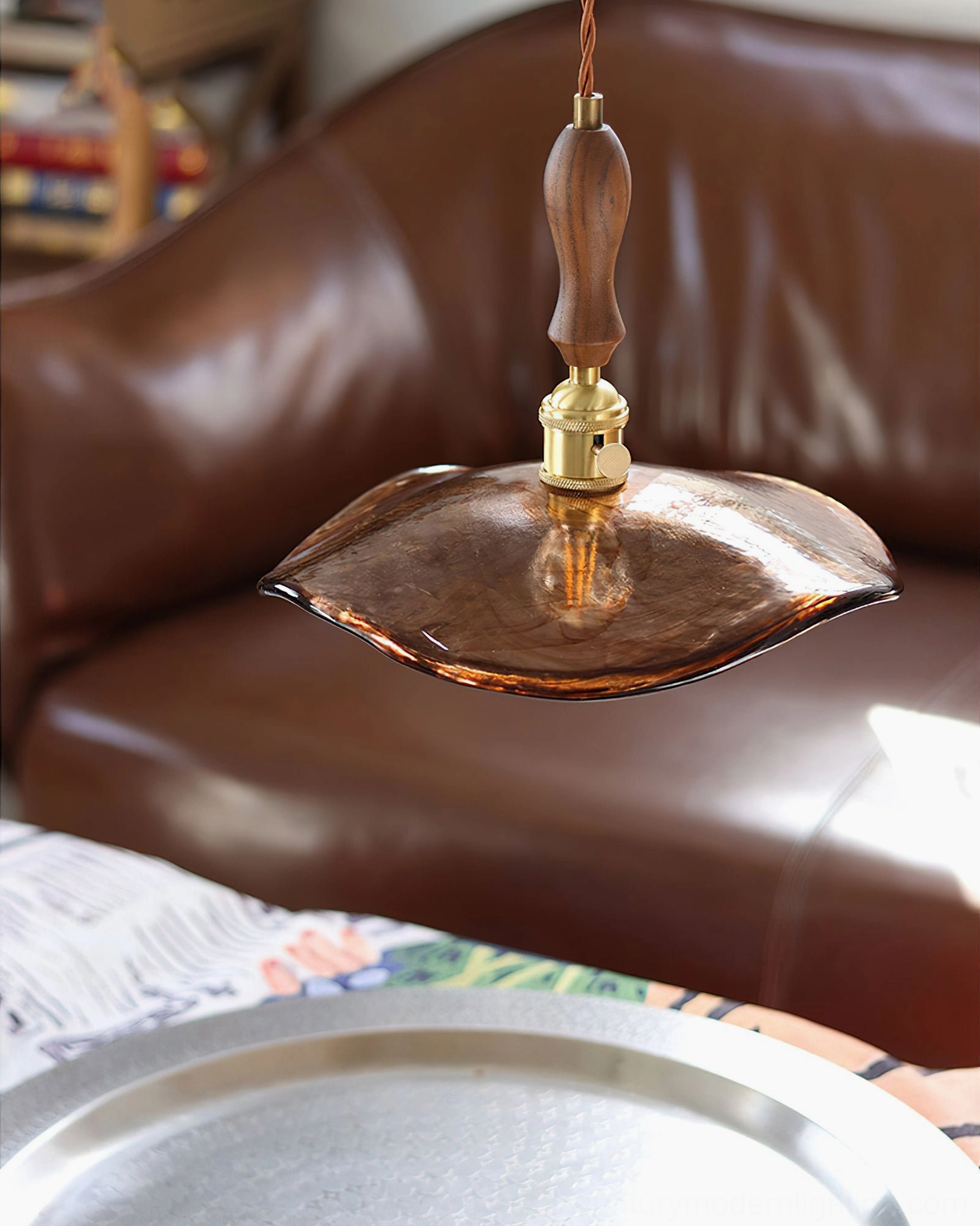 Gideon amber glass pendant hanging above leather sofa lounge with serving tray table, showcasing ambient lighting in upscale vintage interior