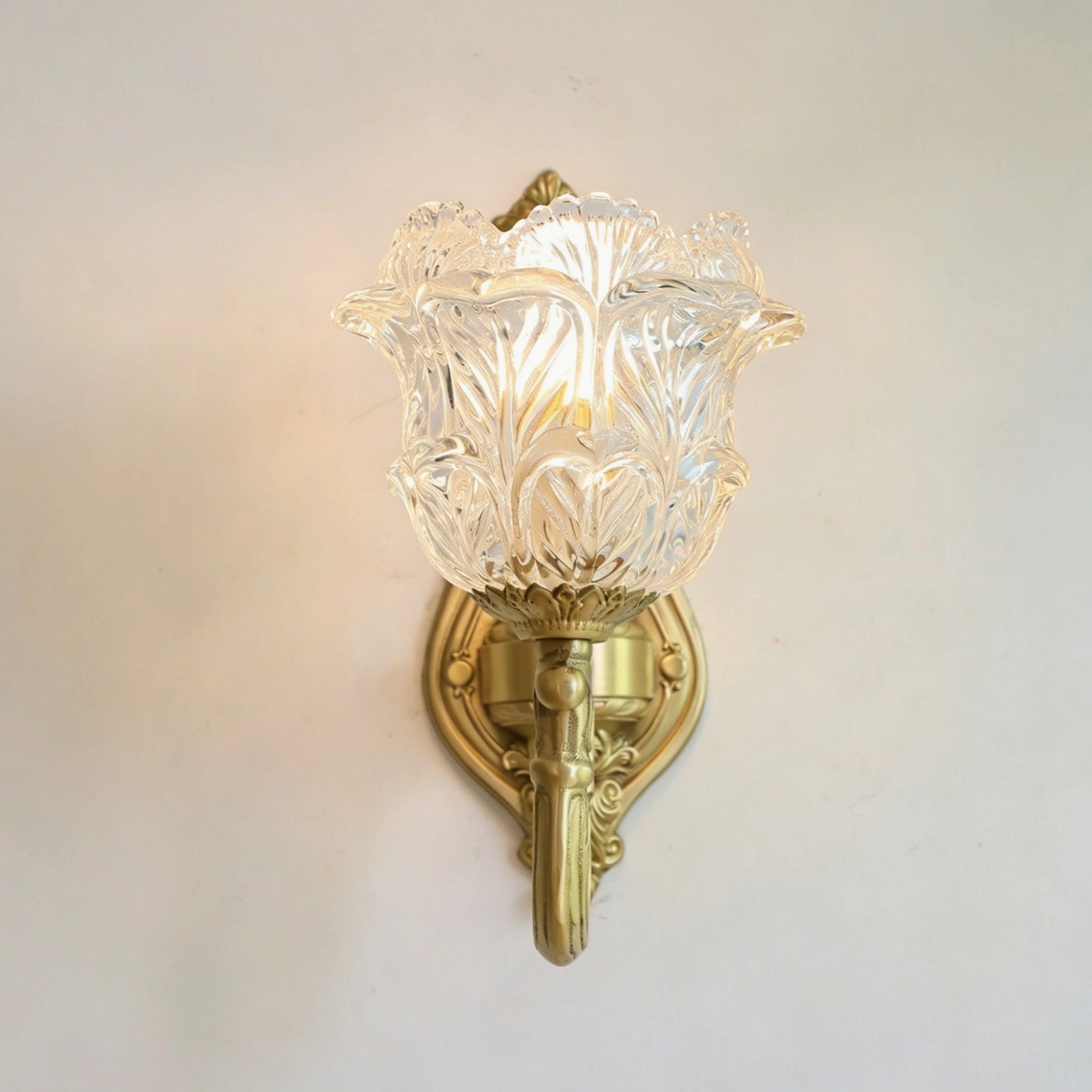 Partial close-up of Gideon Baroque sconce hardware showing intricate carved gold brass metalwork and delicate glass shade detail on white wall