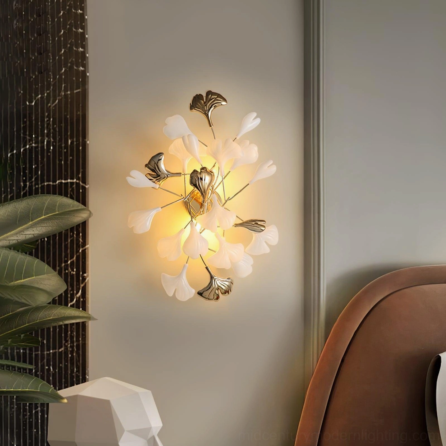 Gold metal ginkgo leaf sconce on modern bedroom wall, oblique view with green houseplant, organic modern interior design
