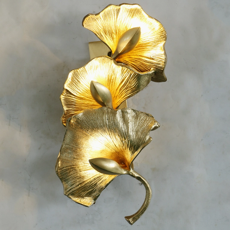 Ginkgo leaf wall sconce glowing warm light grey concrete wall four vertical brass leaves illuminated