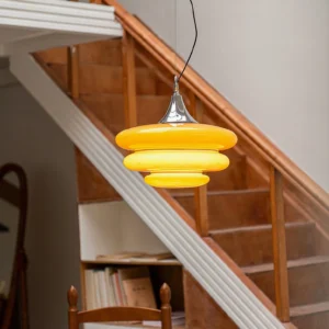 Illuminated orange mid-century pendant light glowing warm yellow above wooden stairwell modern interior