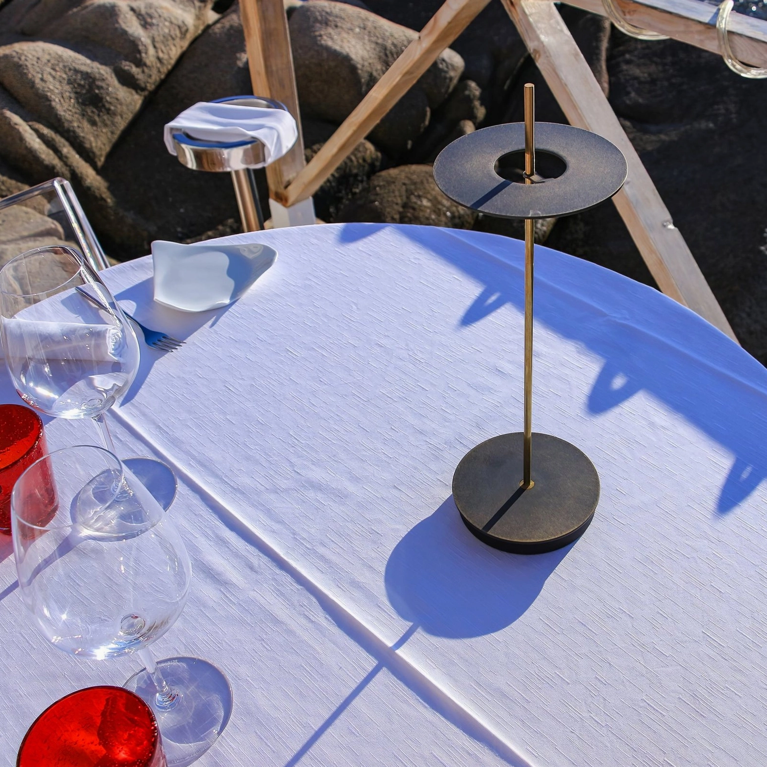 Black Giulietta modern table lamp positioned on oceanfront dining terrace with rocky coastal landscape