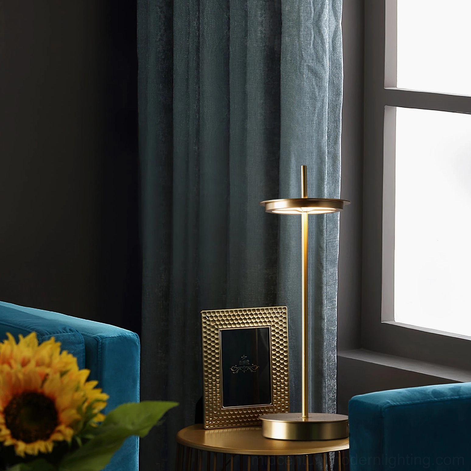 Gold brass Giulietta minimalist table lamp styling on side table next to blue velvet sofa in living room