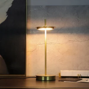 Lit Giulietta table lamp on wooden desk showing warm 3000K ambient glow and polished brass finish, side angle