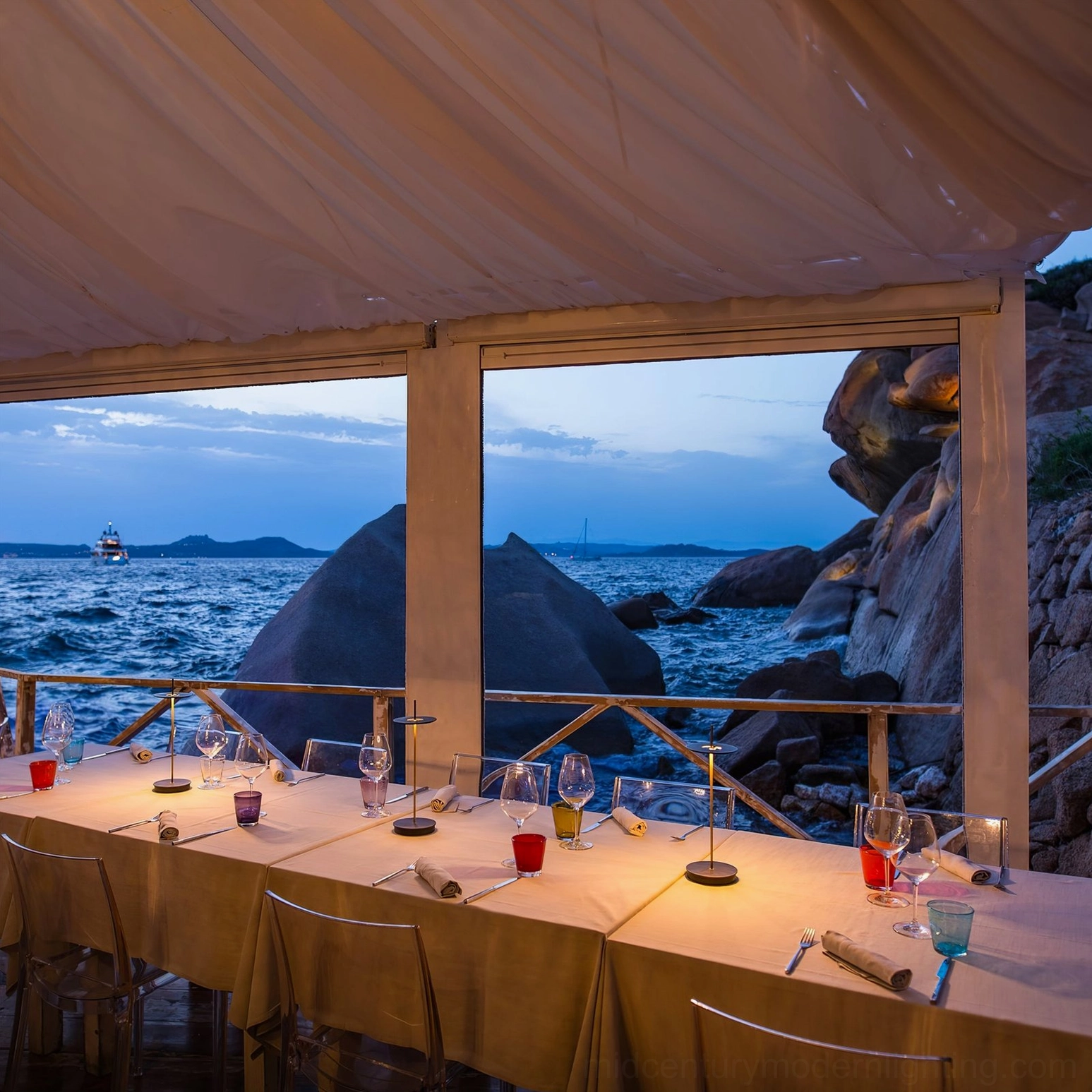 Multiple Giulietta table lamps arranged on outdoor seaside restaurant dining table at dusk with ocean backdrop
