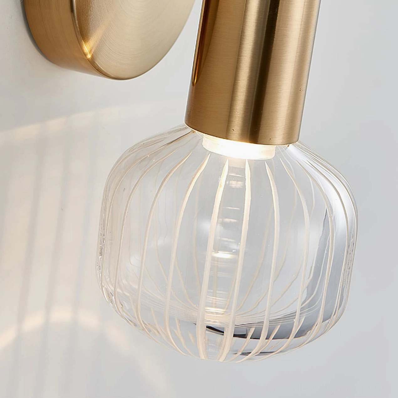 Glaive wall lamp illuminated close-up shot, ribbed spherical glass shade with warm LED light glow