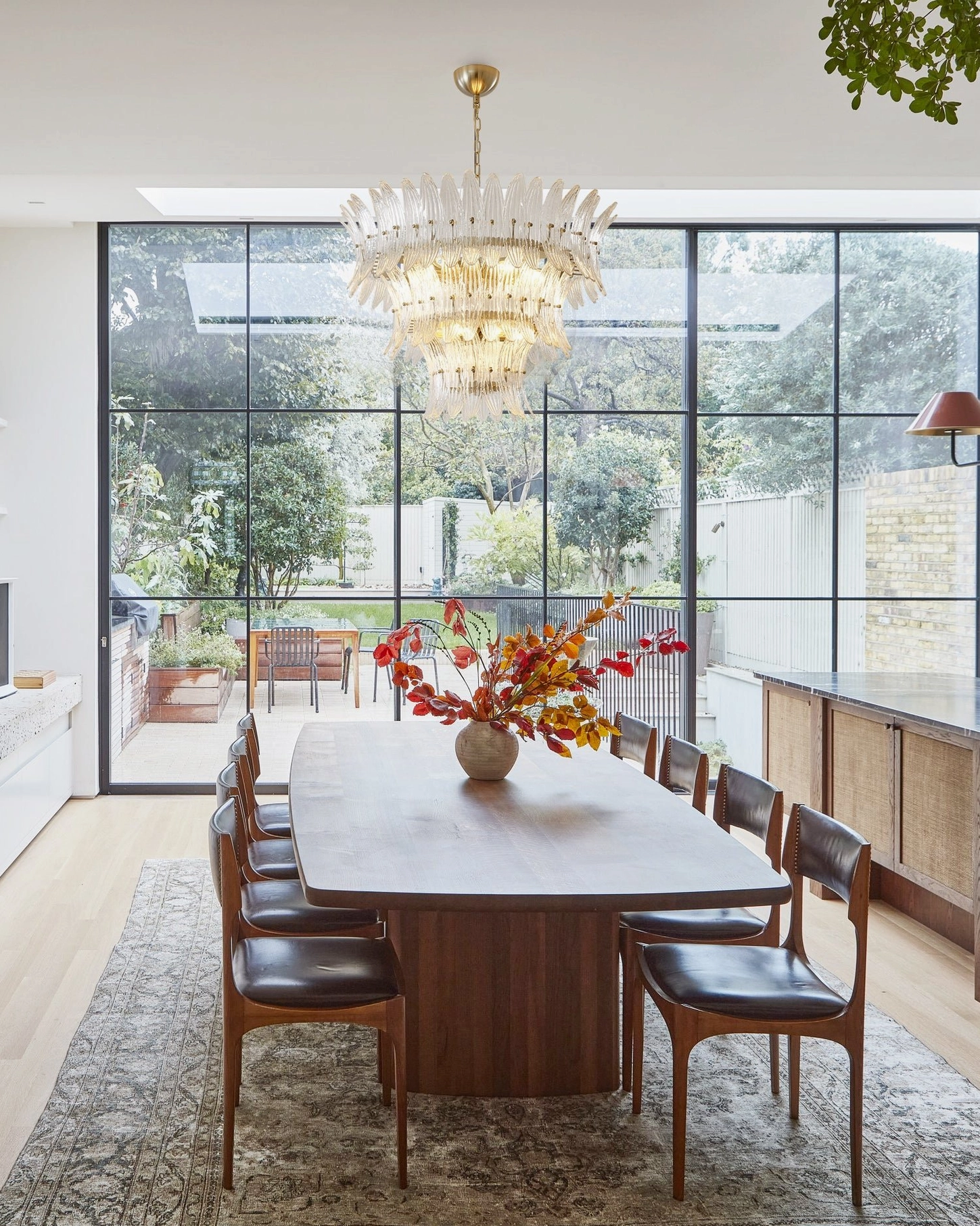 Glass palm chandelier installed in bright contemporary dining room with floor-to-ceiling windows and elegant furnishings