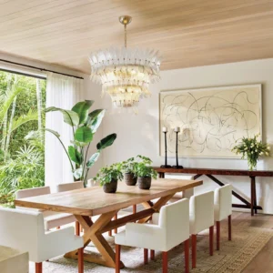 Modern tiered glass palm chandelier illuminated in contemporary dining room with wooden furniture and green plants