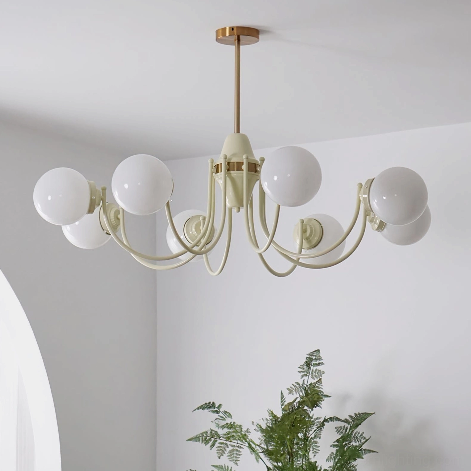 Cream brass globe chandelier with polished gold accents in minimalist room with arched decor and plants