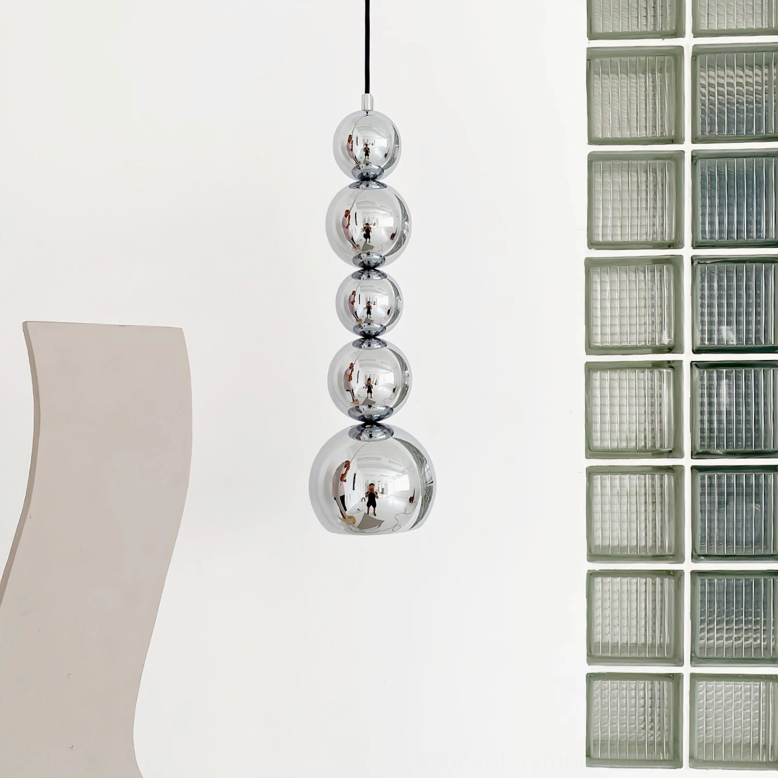 Chrome ball pendant light near glass brick wall, polished silver finish showing vertical hanging design
