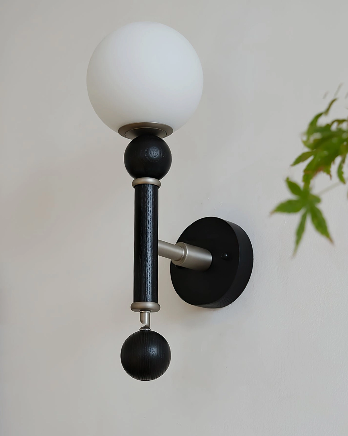 Side angle close-up of globe wall sconce with asymmetrical spherical frosted glass design and foliage backdrop
