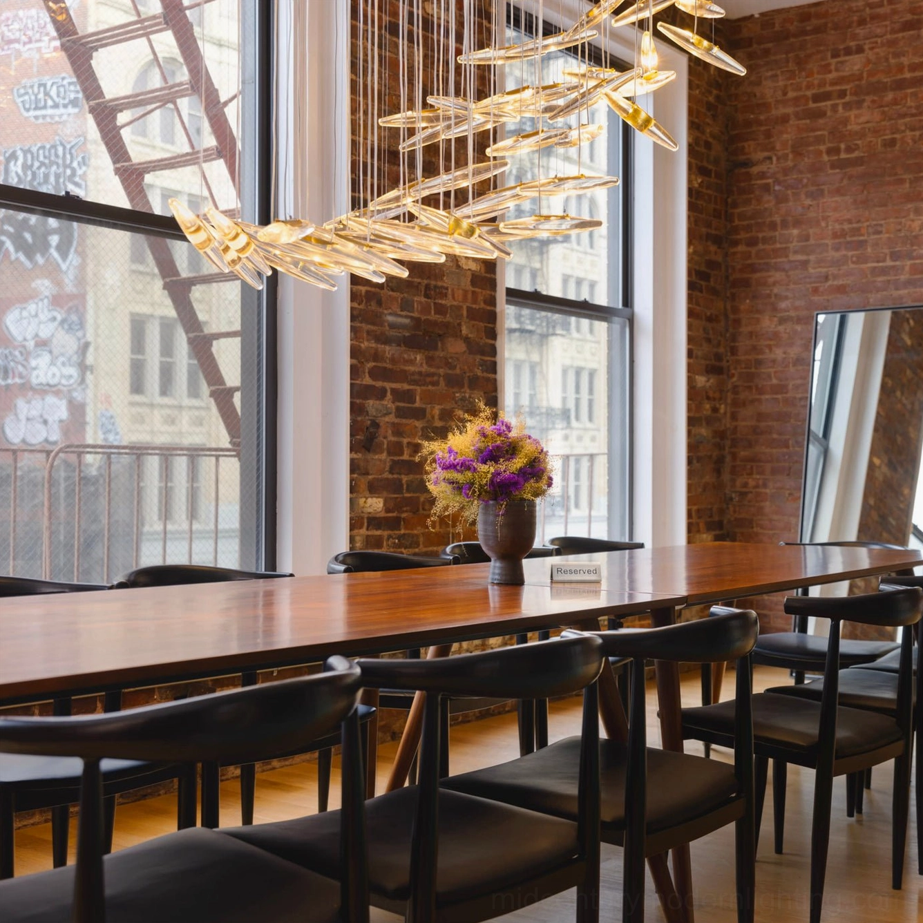 Golden leaf pendant chandelier suspended above long wooden dining table in industrial upscale dining room with exposed brick