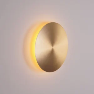 Gossa disc wall lamp mounted on light gray wall emitting warm ambient side glow from beneath circular disc