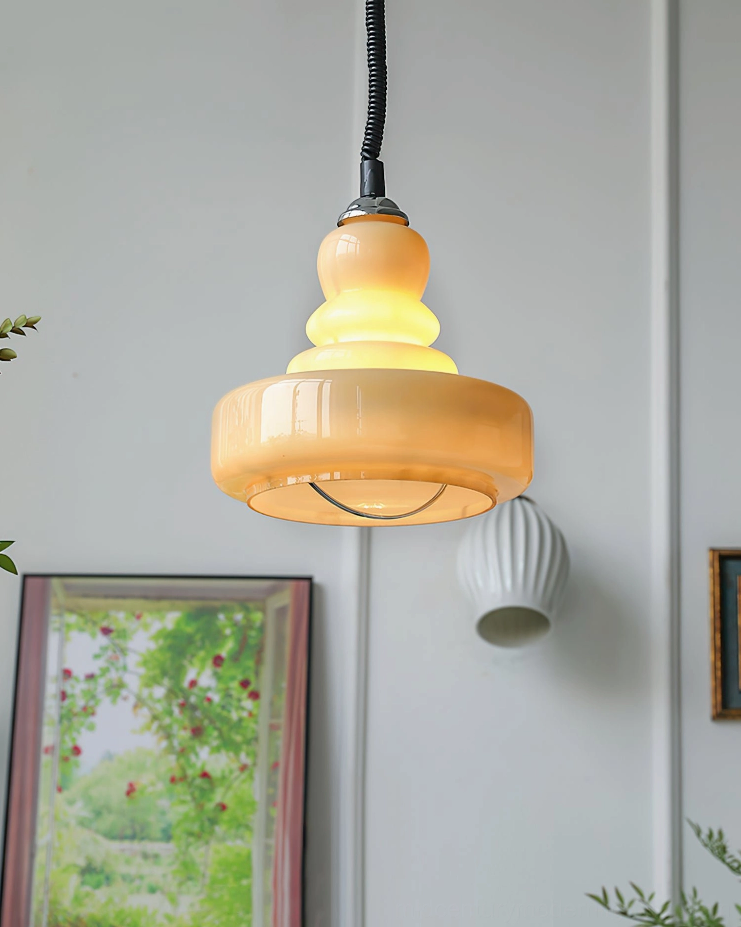 Wide-rimmed beige gourd pendant with tiered top detail photographed from overhead angle with wall art and lamp background