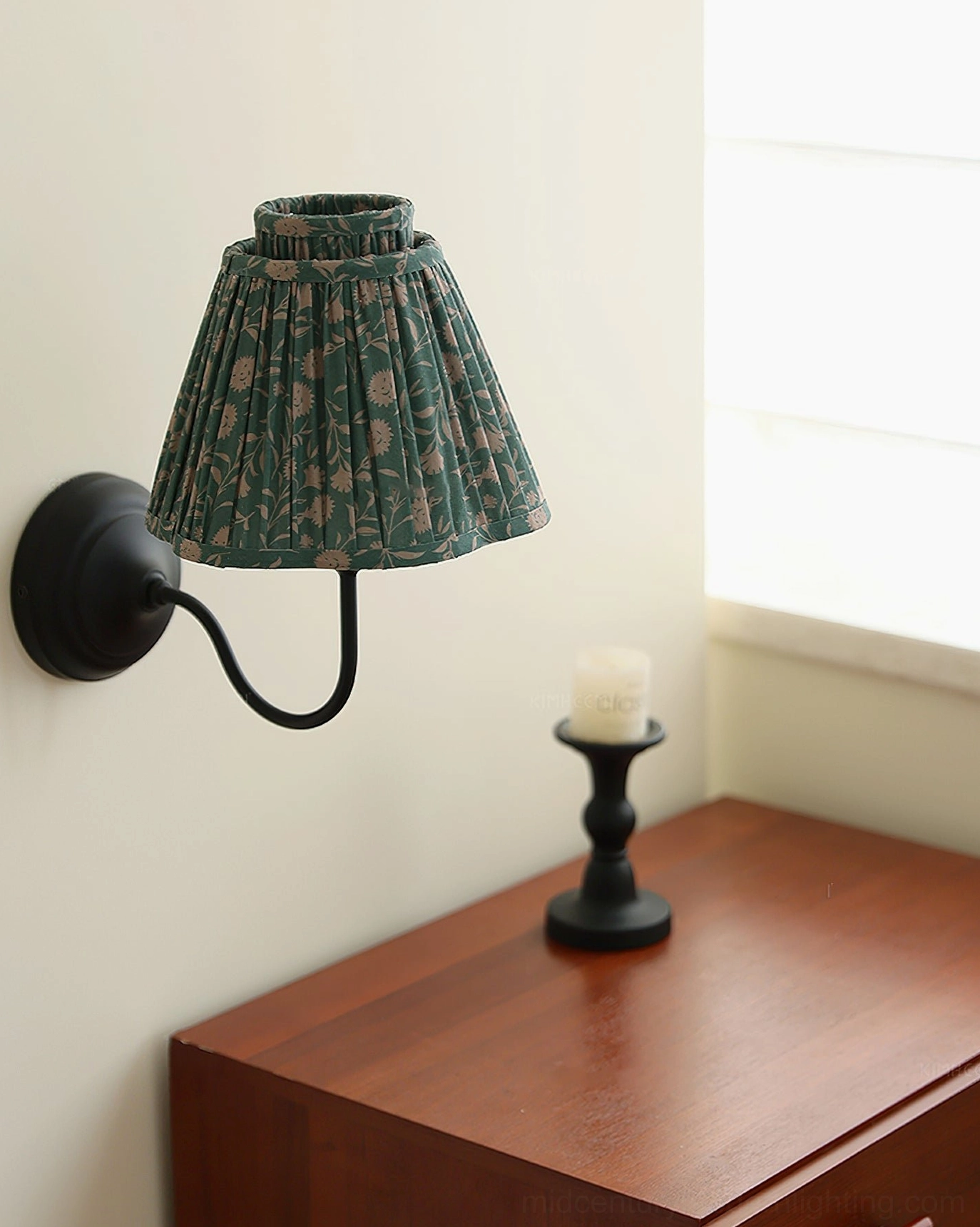 Elbow wall sconce with green pleated shade and black metal bracket, front three-quarter angle with decor