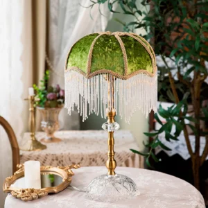 Green shade fringed table lamp displayed on vintage lace dining table with potted plants