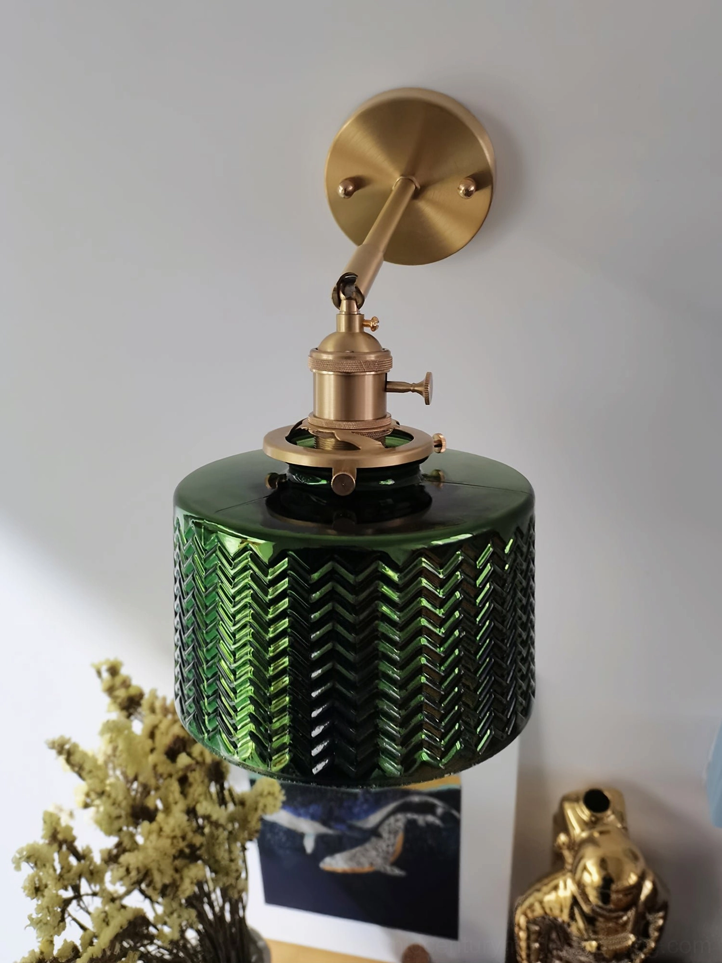 Green glass wall sconce close-up with brass hardware and switch, tabletop styling with home decor