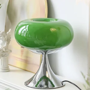 Emerald green lollipop table lamp on decorative shelf with figurines and artwork, showing sculptural disc-on-stem design